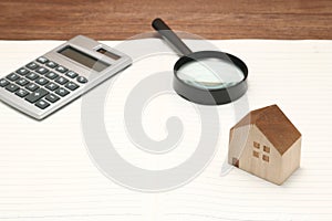 Miniature house, magnifying glass, calculator on blank notebook.