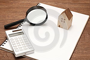 Miniature house, magnifying glass, calculator on blank notebook.