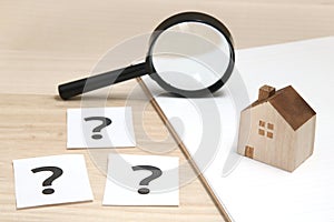 Miniature house and many question marks on white papers. House with question marks and magnifying glass. Real Estate Concept. photo