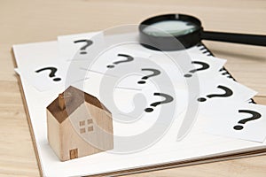 Miniature house and many question marks on white papers. House with question marks and magnifying glass. Real Estate Concept. photo