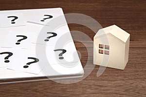 Miniature house and many question marks on white papers. House with question marks.