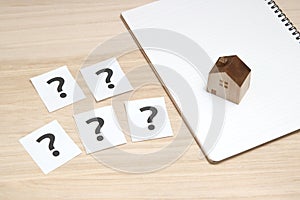 Miniature house and many question marks on white papers. House with question marks.