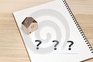 Miniature house and many question marks on white papers. House with question marks.