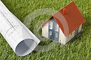 Miniature house model with architectural blueprint on green grass lawn background - house building or buying concept