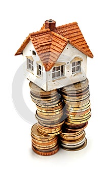 Miniature house perched on stacks of coins symbolizing home finance, AI-generated.