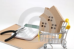 Miniature house, shopping cart, calculator and tools on white background. Concept of buying new house, real estate and renovation.