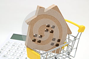 Miniature house, shopping cart and calculator on white background. Concept of buying new house, real estate and home mortgage.
