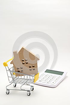 Miniature house, shopping cart and calculator on white background. Concept of buying new house, real estate and home mortgage.