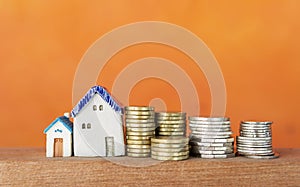 Miniature house and stack of silver and gold coins over blurred orange background