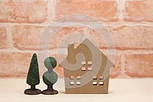 Miniature house and trees in front of brick wall.