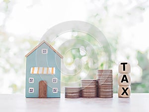 Miniature house, wooden blocks with the word TAX and stack of coins. The concept of paying tax for house and property