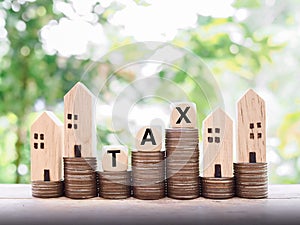 Miniature house, wooden blocks with the word TAX and stack of coins. The concept of paying tax for house and property