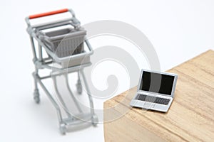 Miniature laptop with small shopping cart on white background.