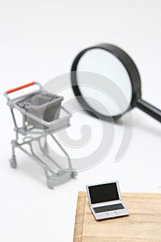 Miniature laptop with small shopping cart on white background.