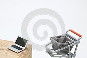 Miniature laptop with small shopping cart on white background.