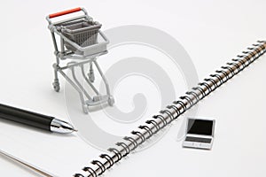 Miniature laptop with small shopping cart on white background.