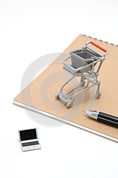 Miniature laptop with small shopping cart on white background.
