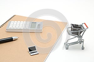 Miniature laptop with small shopping cart on white background.