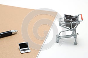 Miniature laptop with small shopping cart on white background.