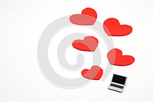 Miniature laptop and some red hearts on white background.