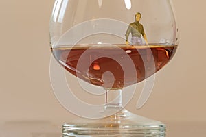 Miniature man figure sinking in the glass of brandy. Shallow depth of field background. Healthcare and alcoholism concept