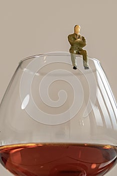 Miniature man figure siting on the glass of brandy. Shallow depth of field background. Healthcare and alcoholism concept