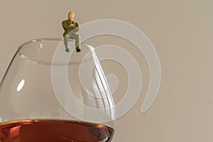Miniature man figure siting on the glass of brandy. Shallow depth of field background. Healthcare and alcoholism concept