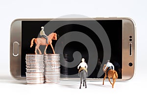 Miniature man riding a horse. Smartphone and pile of coins. photo