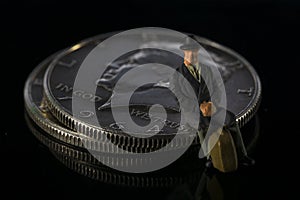 Miniature man seating on Half Dollar coin Black background Macro