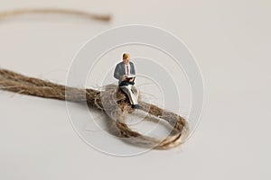 A miniature man sitting on a strapped rope and reading.