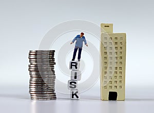 Miniature man standing on the white cubes with RISK word. Miniature and a pile of coins.