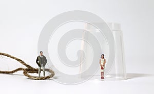 A miniature man tied up with a rope and a miniature woman trapped in a glass.