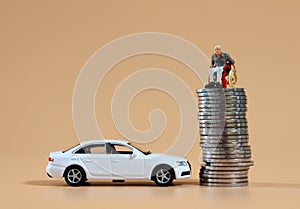 A miniature man in a wheelchair on a pile of coins and a white miniature car. photo