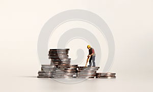 A miniature manual worker on a pile of coins.