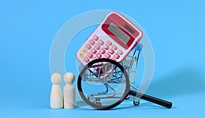 Miniature metal shopping cart with calculator and wooden family, magnifying glass, the concept of budget control, spending on