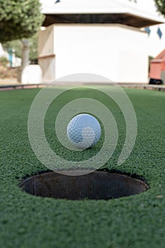 Miniature or mini golf hole close up with ball in center on green artificial turf outdoors portrait view