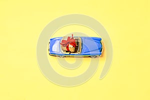 Miniature mini toy.Blue toy car with open top convertible carrying a gift with a red bow on a yellow background. View