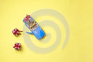 Miniature mini toy.Blue toy car with open top convertible carrying a gift with a red bow on a yellow background. View