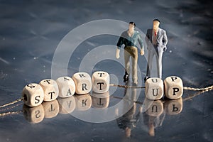 Miniature model of businessmen and wooden cubes with start up inscription strung on a thread