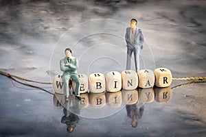 Miniature model of businessmen and wooden cubes with webinar inscription strung on a thread