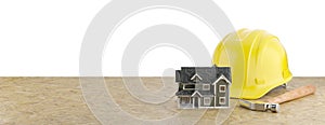 Miniature Model House, Yellow Construction Hard Hat and Hammer Resting on Particleboard Banner Isolated on a White Background photo