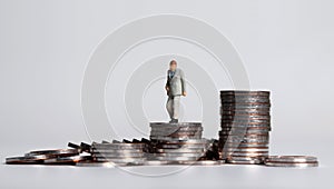 A miniature old age man walking on a pile of coins.