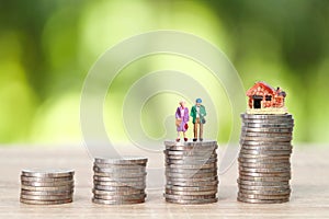Miniature old couple standing on stack coins with house and green background idea for saving money after retire