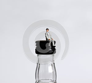 A miniature old man sitting on a liquor bottle top.