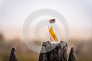 Miniature origami ship in bottle standing on a wooden fence at sunrise