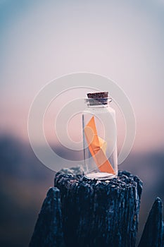 Miniature origami ship in bottle standing on a wooden fence at sunrise