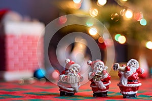 Miniature ornaments of Santa Claus playing musical instruments with blurred decoration and Christmas tree in the background,
