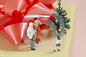 Miniature Parents celebrating christmas with their little boy on top of a gift box