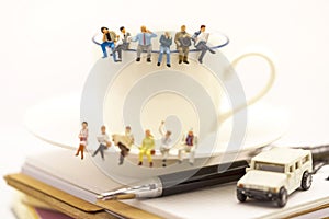 Miniature people: business team sitting on cup of coffee with morning news. Coffee time of business concept