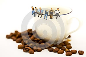 Miniature people: business team sitting on cup of coffee with morning news. Coffee time of business concept